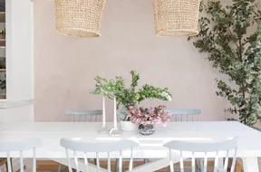 A white dining room table, decorated with two white taper candles and two vases full of flowers